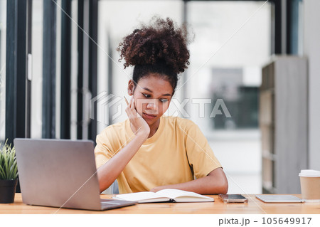 Young African American woman is taking notes in a notebook while watching a webinar video course. Afro american student listening to the lecture to study online through e-learning. Young African American woman is taking notes in a notebook while watching a webinar video course. Afro american student listening to the lecture to study online through e-learning. 105649917