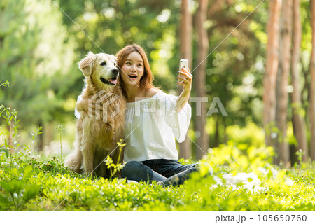 A beautiful young woman taking pictures with her dog on her smartphone in the park 105650760