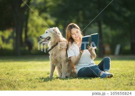 A beautiful young woman reading a book with her dog in the park 105650824