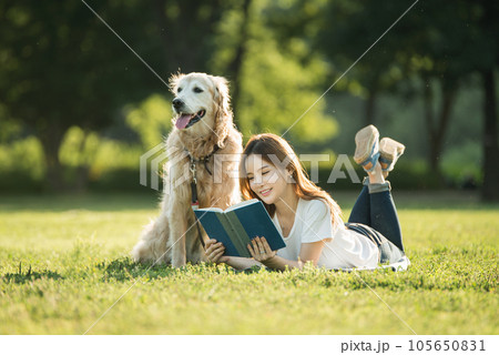 A beautiful young woman reading a book with her dog in the park 105650831