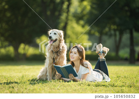 A beautiful young woman reading a book with her dog in the park 105650832
