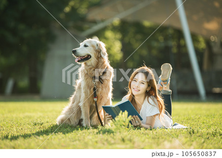 A beautiful young woman reading a book with her dog in the park 105650837