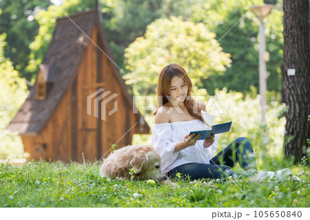 A beautiful young woman reading a book with her dog in the park 105650840