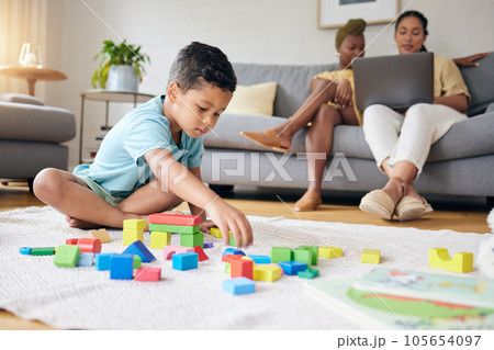 Play, toys and child on floor with parents on sofa for learning, development and education. Lgbtq family, home and boy with building blocks for fun, relax and games with lesbian mothers on laptop 105654097