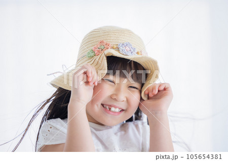 女の子のポートレート　風で飛ばされないように麦わら帽子をおさえる女の子 105654381
