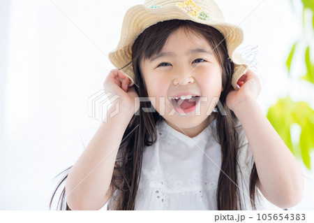 女の子のポートレート　風で飛ばされないように麦わら帽子をおさえる女の子 105654383