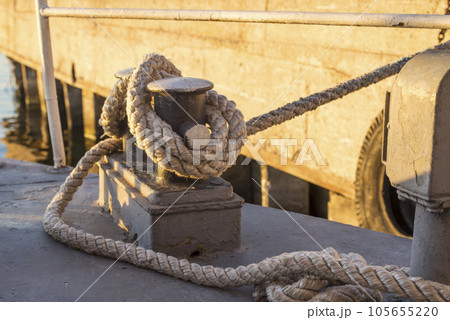 Tied rope knot on metallic bollard seafaring port. Nautical ship moored in dock Tied rope knot on metallic bollard seafaring port. Nautical ship moored in dock 105655220