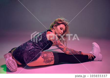 beautiful caucasian blonde girl in velour blue booty shorts and black stockings does stretching on pink background 105655337