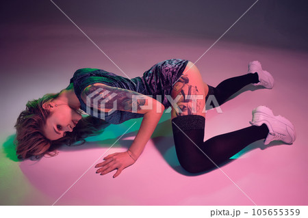 beautiful caucasian blonde girl in velour blue booty shorts and black stockings dancing twerk lying down on pink background 105655359