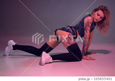 beautiful caucasian blonde girl in velour blue booty shorts and black stockings dancing twerk on her knees on pink background 105655401