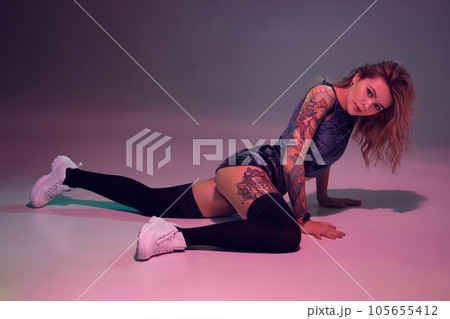 beautiful caucasian blonde girl in velour blue booty shorts and black stockings dancing twerk lying down on pink background 105655412