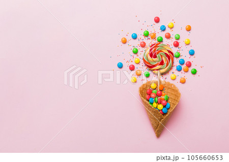 waffle cone full of assorted traditional candies falling out on colored background with copy space. Happy Holidays sale concept waffle cone full of assorted traditional candies falling out on colored background with copy space. Happy Holidays sale concept 105660653