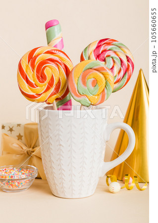 Colorful candies in cup on table on light background background. Large swirled lollipops. Creative concept of a jar full of delicious sweets from the candy store Colorful candies in cup on table on light background background. Large swirled lollipops. Creative concept of a jar full of delicious sweets from the candy store 105660655