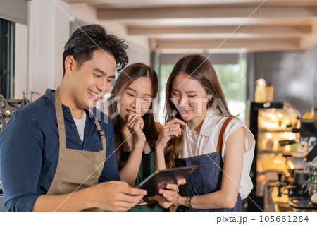 Three barista entrepreneur team meeting at coffee shop. Young smiling Asian male and female cafe employees having discussion on work and menu with tablet computer Three barista entrepreneur team meeting at coffee shop. Young smiling Asian male and female cafe employees having discussion on work and menu with tablet computer 105661284