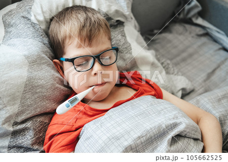A boy with glasses lies on a bed with a thermometer in his mouth. Temperature measurement during a cold A boy with glasses lies on a bed with a thermometer in his mouth. Temperature measurement during a cold 105662525