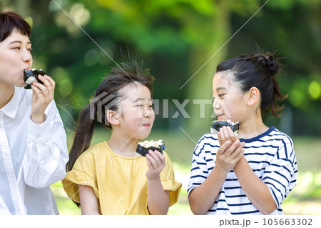 外でおにぎりを食べる大人と子供 外でおにぎりを食べる大人と子供 105663302