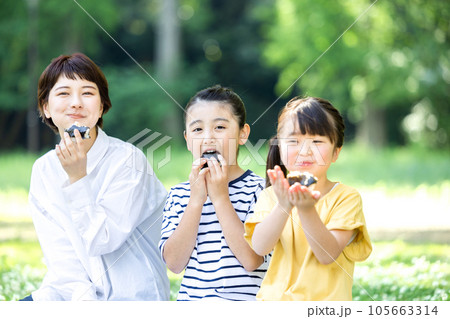 外でおにぎりを食べる大人と子供 105663314
