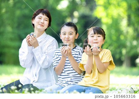 外でおにぎりを食べる大人と子供 105663316