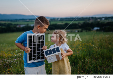 Young boy holding solar panel and his sister holding model of house with installed solar panels. 105664563