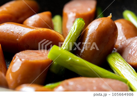 ウインナーソーセージとにんにくの芽をフライパンで炒める調理シーン。 105664986