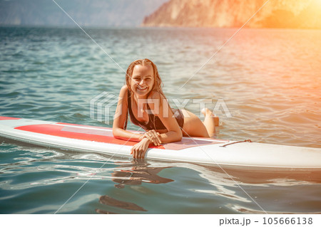Woman sup sea. Sports girl on a surfboard in the sea on a sunny summer day. In a black bathing suit, he sits on a sapa in the sea. Rest on the sea. Woman sup sea. Sports girl on a surfboard in the sea on a sunny summer day. In a black bathing suit, he sits on a sapa in the sea. Rest on the sea. 105666138
