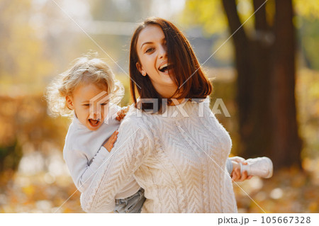 Fashionable mother with daughter. Family in a autumn park. Little girl in a white sweater. 105667328