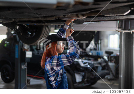 Female mechanic unscrew the nuts on the bottom of the car that is on the lift. A girl at a man's work. 105667458