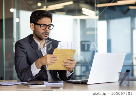 Upset and disappointed businessman at workplace received mail message envelope letter with bad news, arab unhappy with financial results achievement at workplace inside office. Upset and disappointed businessman at workplace received mail message envelope letter with bad news, arab unhappy with financial results achievement at workplace inside office. 105667503