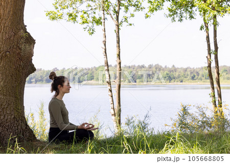 Serenity in Nature: Young Woman Meditating by the Forest Lake Serenity in Nature: Young Woman Meditating by the Forest Lake 105668805