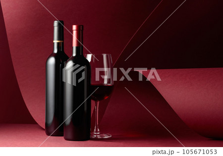 Bottles and glass of red wine on a red background. 105671053