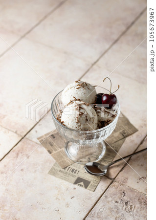 Ice cream in balls with cherry and chocolate in glass bowl on beige tile background, summer refreshing morning dessert, vertical 105673967