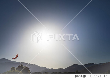 京都の初秋、野焼きの煙たなびく嵯峨野の田園の空に、秋の実りを守る鳥よけの凧が舞う 105674012