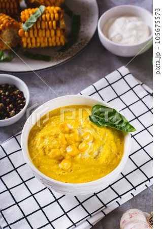 Homemade corn soup with spices and basil in a bowl on the table vertical view 105675573