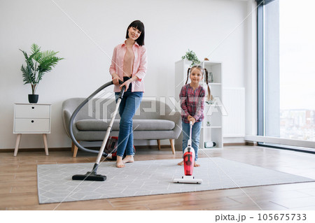 Lady and girl standing with cleaning devices in living room Lady and girl standing with cleaning devices in living room 105675733