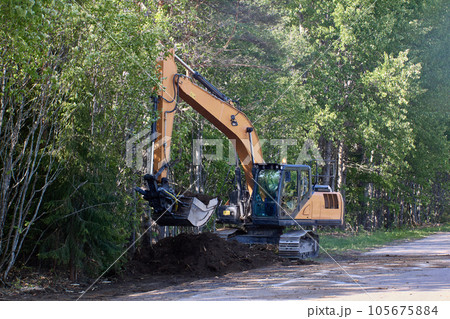 Backhoe deepens drainage ditch on country road. 105675884