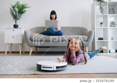 Kid watching robot vacuum cleaning when mom doing remote job Kid watching robot vacuum cleaning when mom doing remote job 105676299
