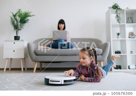 Kid watching robot vacuum cleaning when mom doing remote job Kid watching robot vacuum cleaning when mom doing remote job 105676300