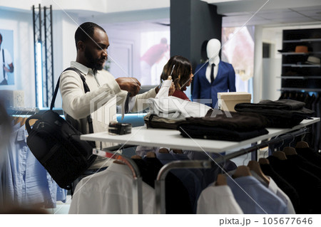 Customer examining tie and shirt match while shopping in clothing store. African american man choosing formal apparel and accessory, checking garment size and style in showroom 105677646