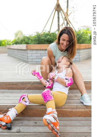 Little girl in roller skates and her mom sit on a wooden ladder and hug outdoors.  105679741