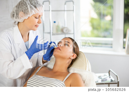 Adult woman cosmetologist makes injection in lips of patient 105682026