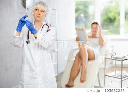Adult female doctor posing with syringe in medical room Adult female doctor posing with syringe in medical room 105682223
