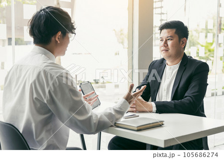 Asian young adult sitting at desk across from manager being interviewed job interview in business room. Asian young adult sitting at desk across from manager being interviewed job interview in business room. 105686274