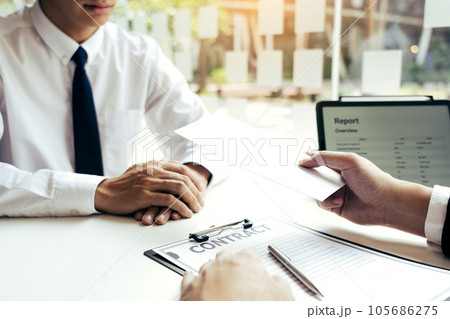 Male manager is talking or explaining about having to dismiss the employee while being handed out a resignation envelope to the employee. 105686275