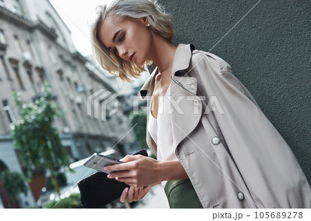 Fashion. Young stylish woman standing on the city street using application on smartphone concentrated close-up Fashion. Young stylish woman standing on the city street using application on smartphone concentrated close-up 105689278