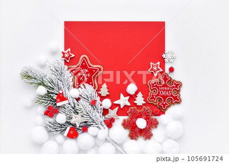 Spruce branch in the snow with Christmas decorations on white and red background.  105691724