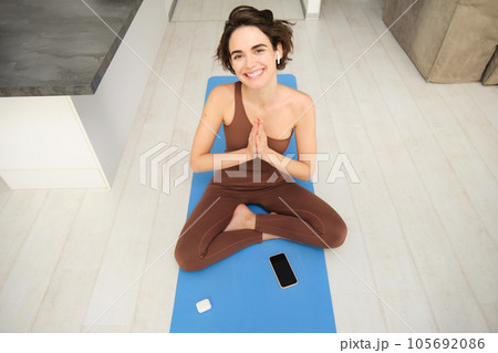 Beautiful cute sporty woman doing exercise in bright room. Focused on brunette sitting on the floor practicing yoga wear top and leggings. Home mood, lifestyle Beautiful cute sporty woman doing exercise in bright room. Focused on brunette sitting on the floor practicing yoga wear top and leggings. Home mood, lifestyle 105692086