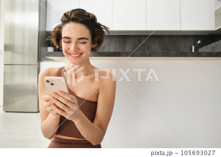 Portrait of smiling woman at home, using her mobile phone, sitting on floor in bright room, looking at smartphone and chatting, texting someone Portrait of smiling woman at home, using her mobile phone, sitting on floor in bright room, looking at smartphone and chatting, texting someone 105693027