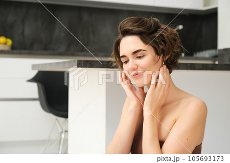 Close up of young smiling brunette woman, fitness girl in kitchen, looks aside, touches her face, listens to mindful app training session in wireless earphones, workout at home 105693173