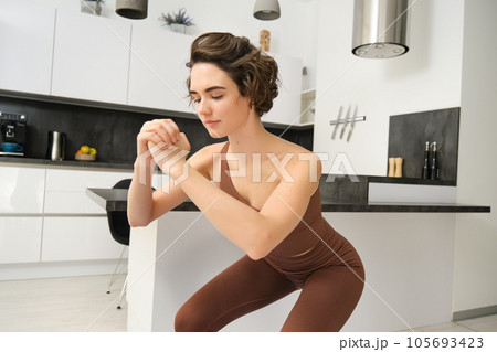 Workout and women wellbeing concept. Young fitness woman, doing squats, workout from home without gym equipment, training in bright room 105693423
