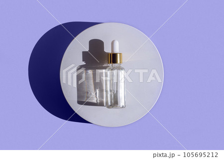 Natural oil cosmetics on violet background. Dropper glass Bottle Mock-Up. Oily cosmetic pipette. Face and body treatment, spa concept. Mineral organic oil. Top view. Beauty products. Blank bottle 105695212